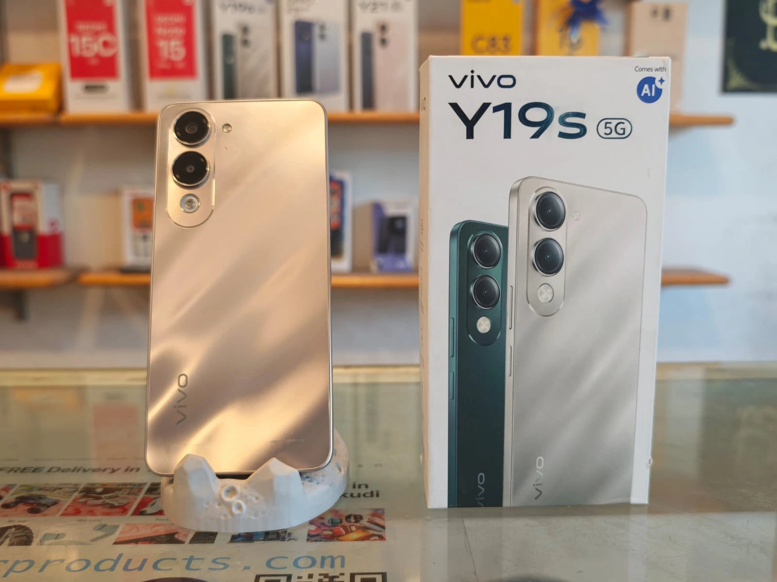 Vivo Y19s 5G smartphone in Titanium Gold color with retail box, featuring 4GB RAM, 64GB storage, Dimensity 6300 processor, 13MP AI camera, and 6000mAh battery.